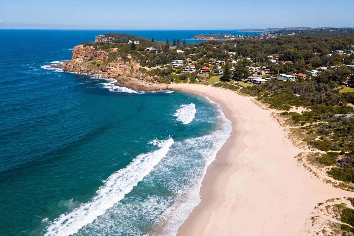 The New South Wales northern beaches coastline from above, sandstone headland, pale sand and deep teal ocean with white surf lines